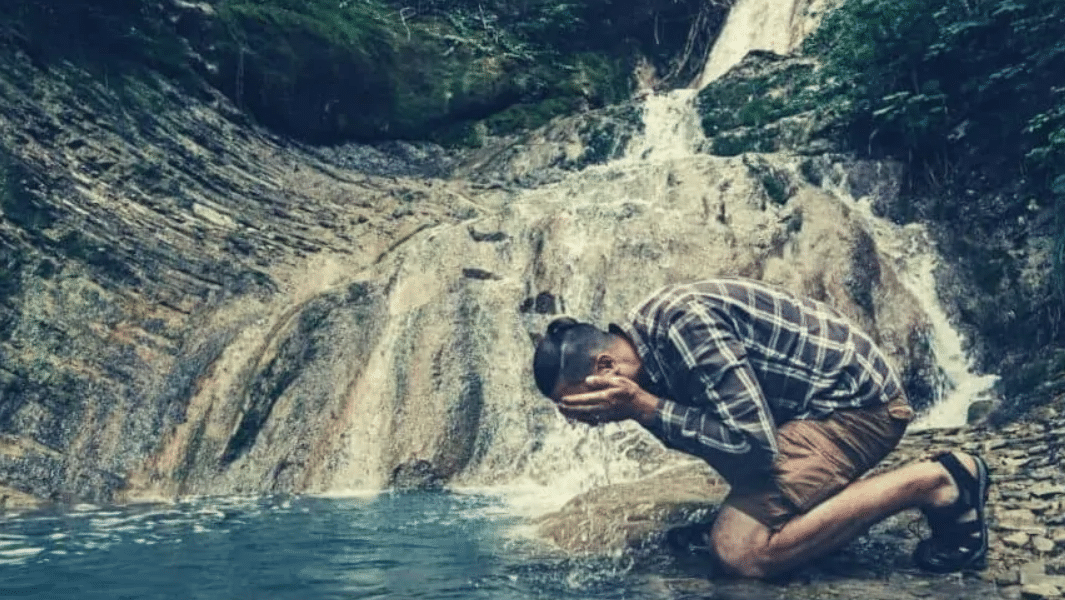 A Young Hiker Kneels By The Falls And Washed His Face